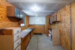 Kitchen with unfinished concrete floors, wood walls, brown cabinetry, and light countertops