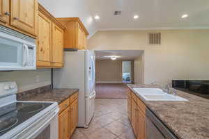 Kitchen featuring white appliances, ornamental molding, light tile patterned flooring, recessed lighting, and dark countertops