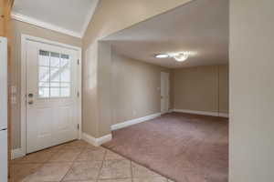 Foyer featuring crown molding, light colored carpet, vaulted ceiling, and light tile patterned floors