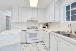 Kitchen featuring white appliances, white cabinetry, light countertops, under cabinet range hood, and a peninsula