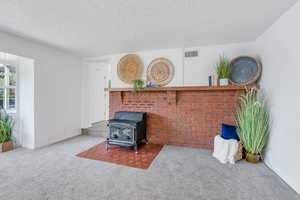 Carpeted living area with a wood stove and a textured ceiling