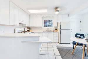 Kitchen with white appliances, a peninsula, light countertops, light tile patterned flooring, and under cabinet range hood