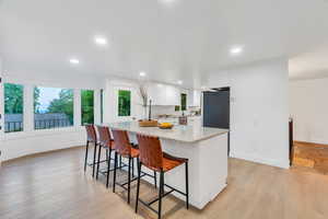 Kitchen featuring a breakfast bar area, white cabinetry, light wood-style floors, light stone counters, and decorative backsplash