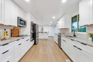 Kitchen featuring tasteful backsplash, light wood-type flooring, recessed lighting, white cabinets, and appliances with stainless steel finishes