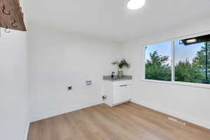 Laundry area featuring hookup for a washing machine, electric dryer hookup, light wood finished floors, and cabinet space