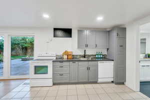 Kitchen featuring gray cabinets, white appliances, dark countertops, light tile patterned flooring, and recessed lighting