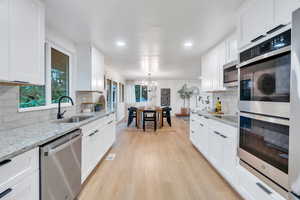 Kitchen featuring stainless steel appliances, a chandelier, light wood-type flooring, white cabinets, and backsplash