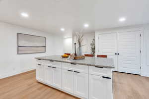 Kitchen featuring white cabinets, light wood-style floors, light stone countertops, recessed lighting, and a kitchen island