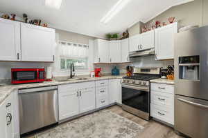 Kitchen with stainless steel appliances, light wood-style flooring, ornamental molding, light countertops, and under cabinet range hood