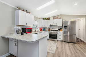 Kitchen featuring stainless steel appliances, lofted ceiling, light countertops, a peninsula, and light wood finished floors
