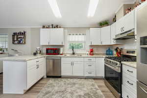 Kitchen with appliances with stainless steel finishes, a peninsula, crown molding, light wood-style flooring, and under cabinet range hood