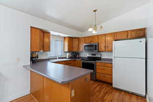 Kitchen with appliances with stainless steel finishes, vaulted ceiling, brown cabinets, dark wood finished floors, and a peninsula