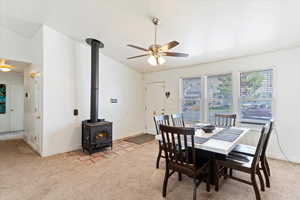 Dining space with a wood stove, light carpet, ceiling fan, and a textured ceiling