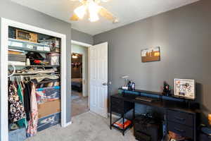 Bedroom featuring carpet flooring, an office area, a textured ceiling, a ceiling fan, and a closet