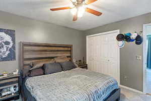 Carpeted bedroom with a textured ceiling, a closet, and a ceiling fan