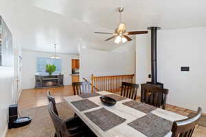 Dining room featuring lofted ceiling, light wood-style floors, a fireplace, ceiling fan, and a textured ceiling