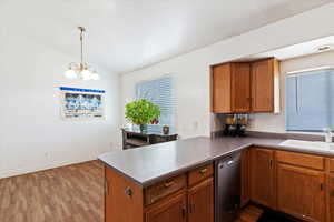 Kitchen with vaulted ceiling, brown cabinets, wood finished floors, dishwasher, and a peninsula