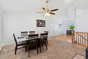 Dining space featuring light colored carpet, vaulted ceiling, a chandelier, a ceiling fan, and light wood finished floors
