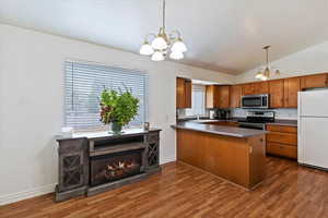 Kitchen with brown cabinets, a chandelier, stainless steel appliances, lofted ceiling, and a peninsula