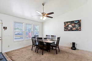 Dining room featuring vaulted ceiling, light colored carpet, a textured ceiling, and a ceiling fan