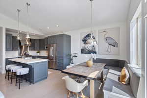 Kitchen with lofted ceiling, light countertops, light wood-style flooring, appliances with stainless steel finishes, and an island with sink