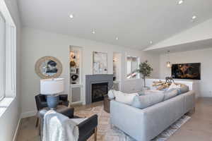 Living area with lofted ceiling, recessed lighting, light wood-style floors, a glass covered fireplace, and built in shelves