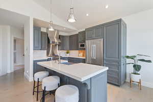 Kitchen featuring lofted ceiling, appliances with stainless steel finishes, light countertops, light wood-style flooring, and wall chimney exhaust hood