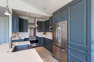 Kitchen with vaulted ceiling, high end appliances, wall chimney range hood, tasteful backsplash, and light wood-type flooring