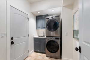 Laundry area featuring estacked washer and dryer, cabinet space, recessed lighting, and stone finish floors