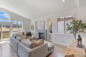 Living area featuring lofted ceiling, plenty of natural light, light wood-type flooring, a glass covered fireplace, and recessed lighting