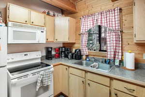 Kitchen featuring white appliances, light brown cabinetry, wooden walls, and light countertops