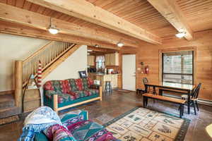 Living area with stairway, a wood ceiling with exposed beams, wooden walls, and stone tile flooring