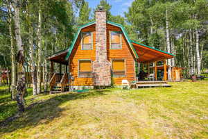 Back of property with a lawn, a gambrel roof, a chimney, an outdoor structure, and a deck
