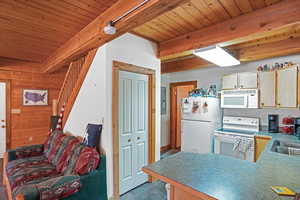 Kitchen with a wood ceiling with exposed beams, white appliances, a peninsula, wooden walls, and tile patterned floors