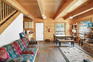 Living area with wood walls, a wood ceiling with exposed beams, and stone tile flooring