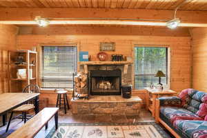 Living area with wooden walls, a stone fireplace, and a wood ceiling with exposed beams