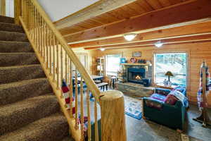Living area with healthy amount of natural light, stone finish flooring, wooden walls, a stone fireplace, and stairs