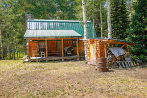 Rear view of property featuring log veneer siding, a chimney, and a metal roof