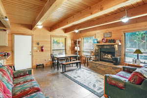 Living area featuring wooden walls, a wooden ceiling with exposed beams, and a stone fireplace