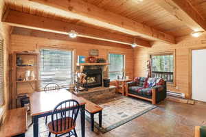 Living area with wooden walls, a wooden ceiling with exposed beams, a fireplace, stone finish floors, and a baseboard radiator