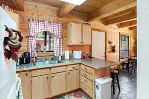 Kitchen featuring light brown cabinets, wood walls, a wood ceiling with exposed beams, a peninsula, and a breakfast bar