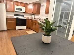 Kitchen featuring white appliances, wood finish cabinetry, light wood finished floors, and light stone countertops