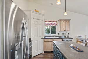 Kitchen featuring appliances with stainless steel finishes, light brown cabinetry, dark wood-type flooring, vaulted ceiling, and dark countertops