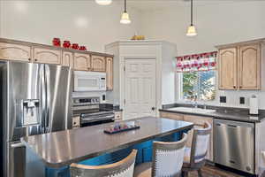 Kitchen featuring appliances with stainless steel finishes, dark countertops, a breakfast bar, a kitchen island, and hanging light fixtures