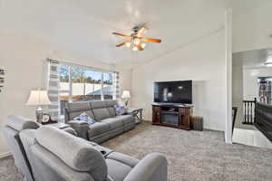 Living area with vaulted ceiling, carpet floors, a ceiling fan, and a fireplace