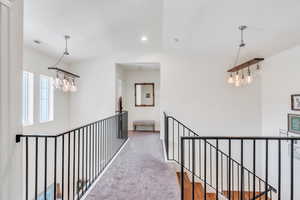 Corridor with an upstairs landing, a chandelier, lofted ceiling, and carpet