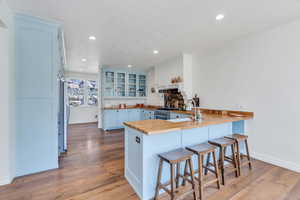 Kitchen featuring a peninsula, butcher block counters, wood finished floors, a kitchen breakfast bar, and blue cabinetry