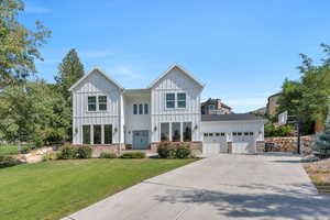 Modern farmhouse style home featuring board and batten siding, a front lawn, an attached garage, and driveway