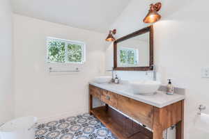 Bathroom with double vanity, lofted ceiling, and tile patterned flooring