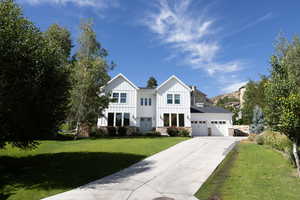 Modern farmhouse with board and batten siding, driveway, a front yard, a garage, and stone siding